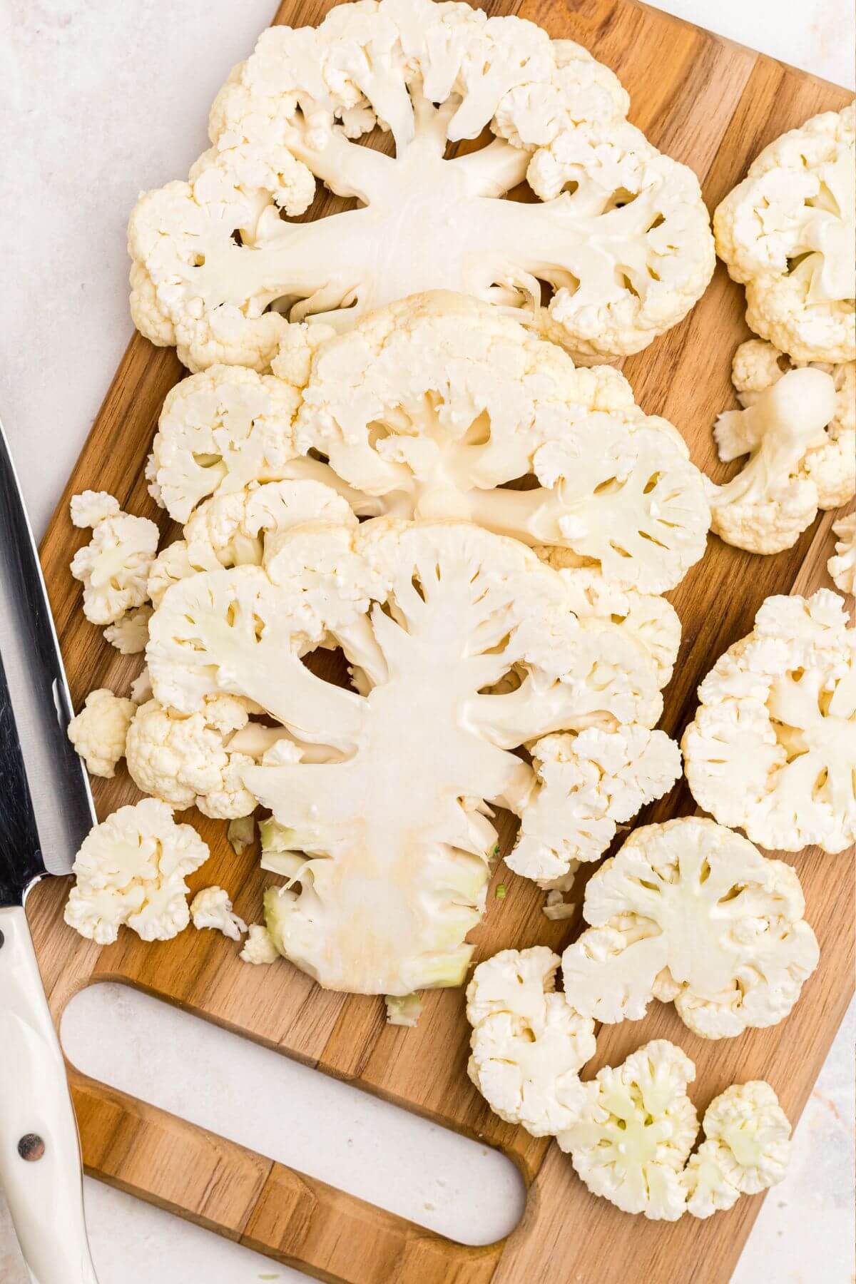 Uncooked cauliflower cut into slabs on a wooden cutting board. 
