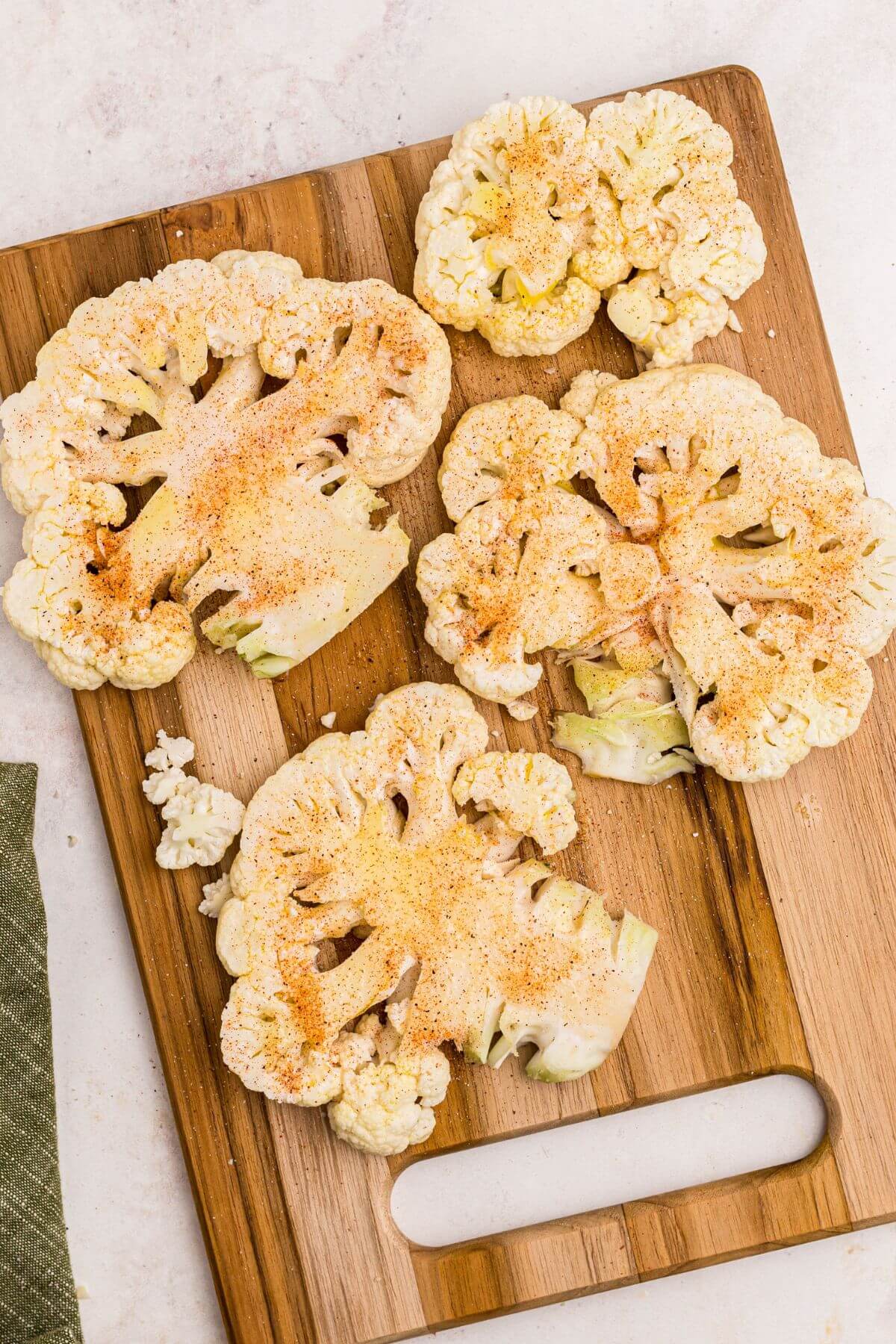 Seasoned uncooked cauliflower steaks on a wooden cutting board before being air fried. 