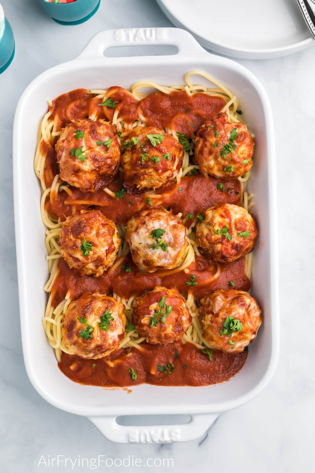 Air fryer chicken meatballs topped with marinara sauce and cheese and served over a dish of spaghetti noodles. 