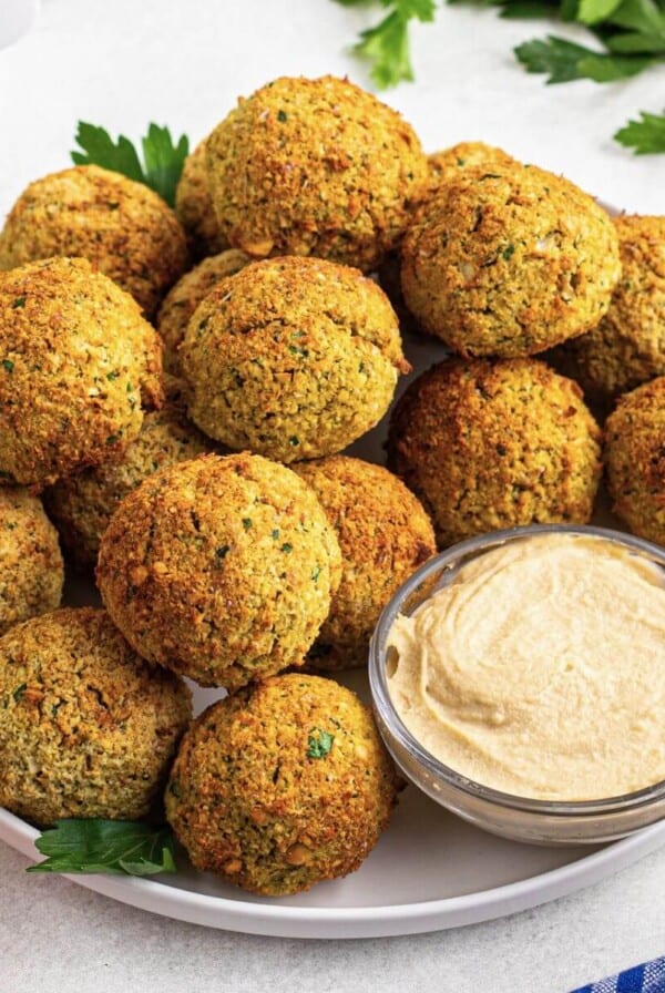 Golden brown falafels stacked on a white plate served with hummus