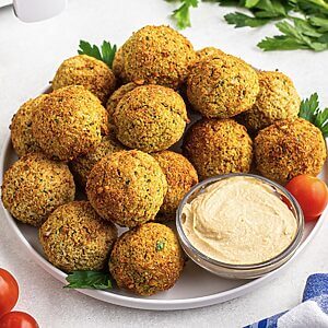 Golden brown falafels stacked on a white plate served with hummus