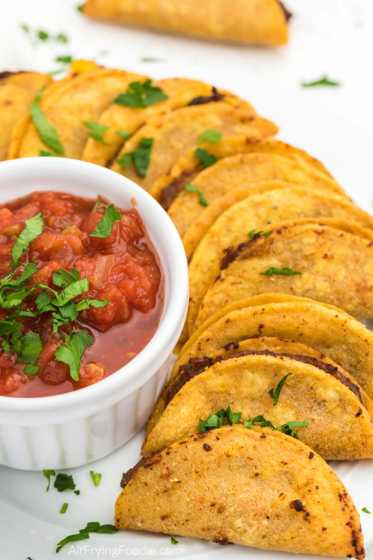 Air fried mini tacos on a white plate with salsa for dipping. 