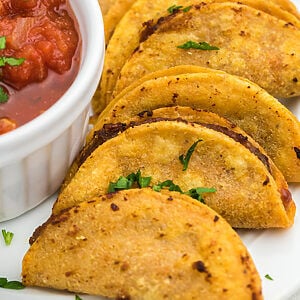 Air fried mini tacos served on a white plate with a side of salsa for dipping.