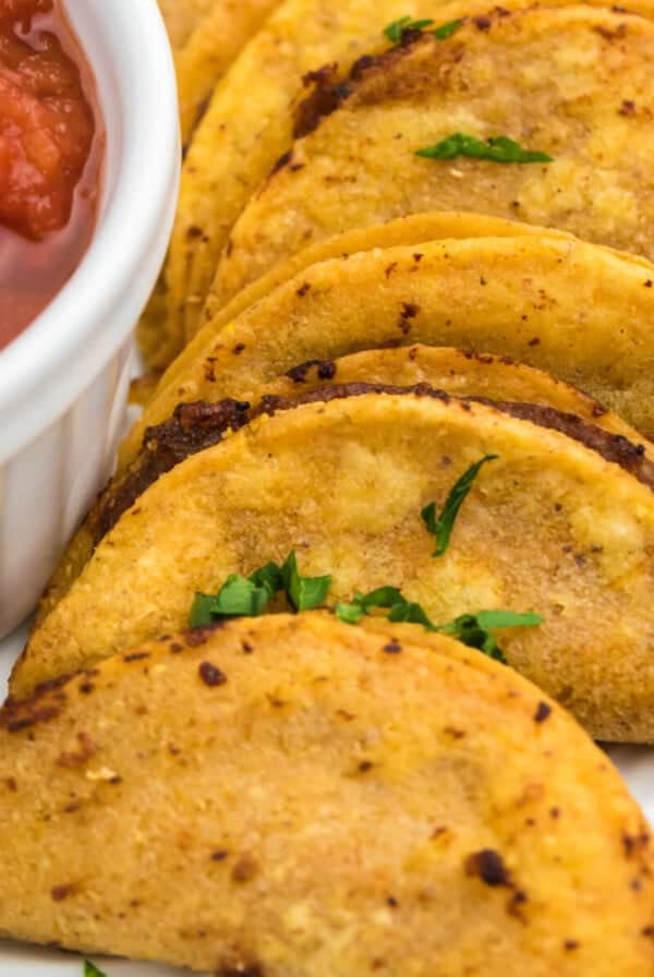 Air fried mini tacos served on a white plate with a side of salsa for dipping.