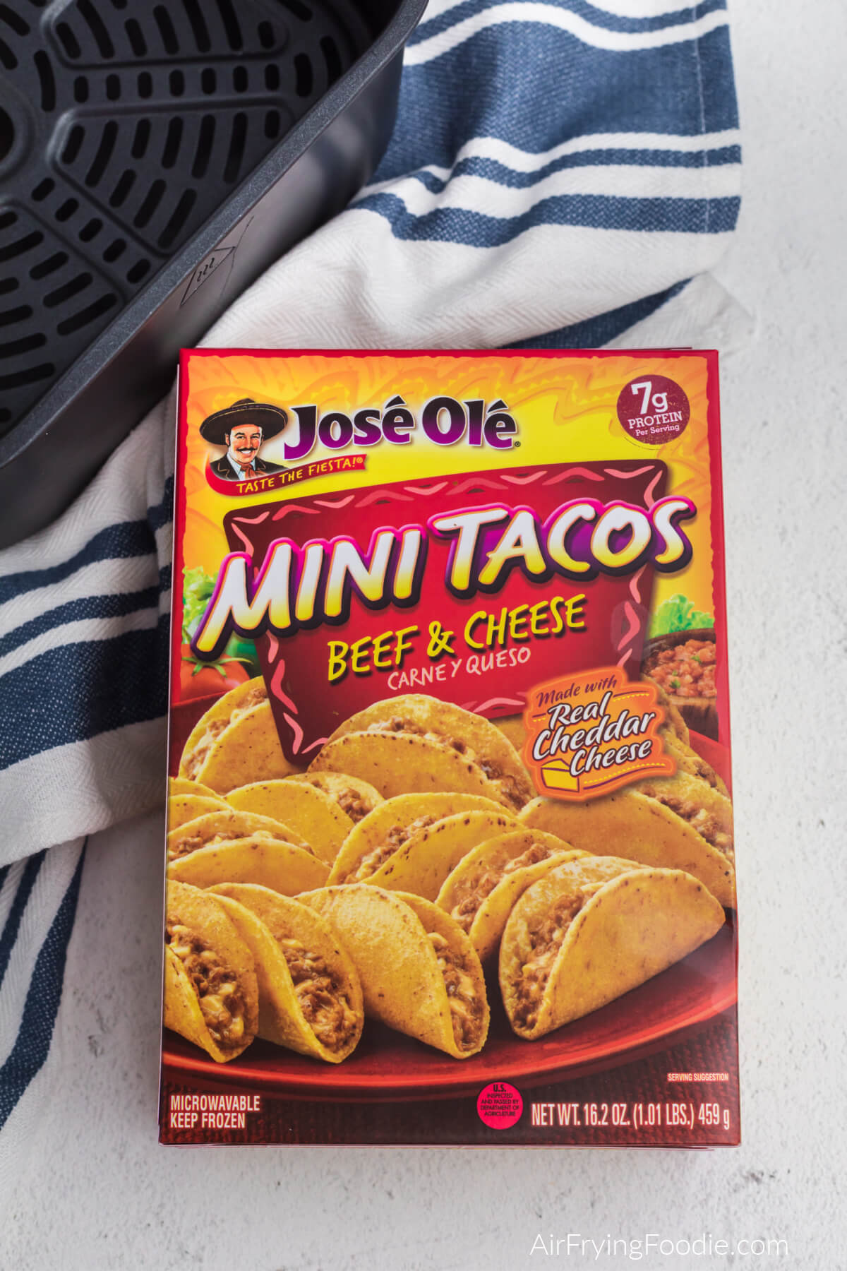 Box of Jose Ole frozen mini tacos made with beef and cheese in the box on a counter with a towel and the basket of the air fryer. 