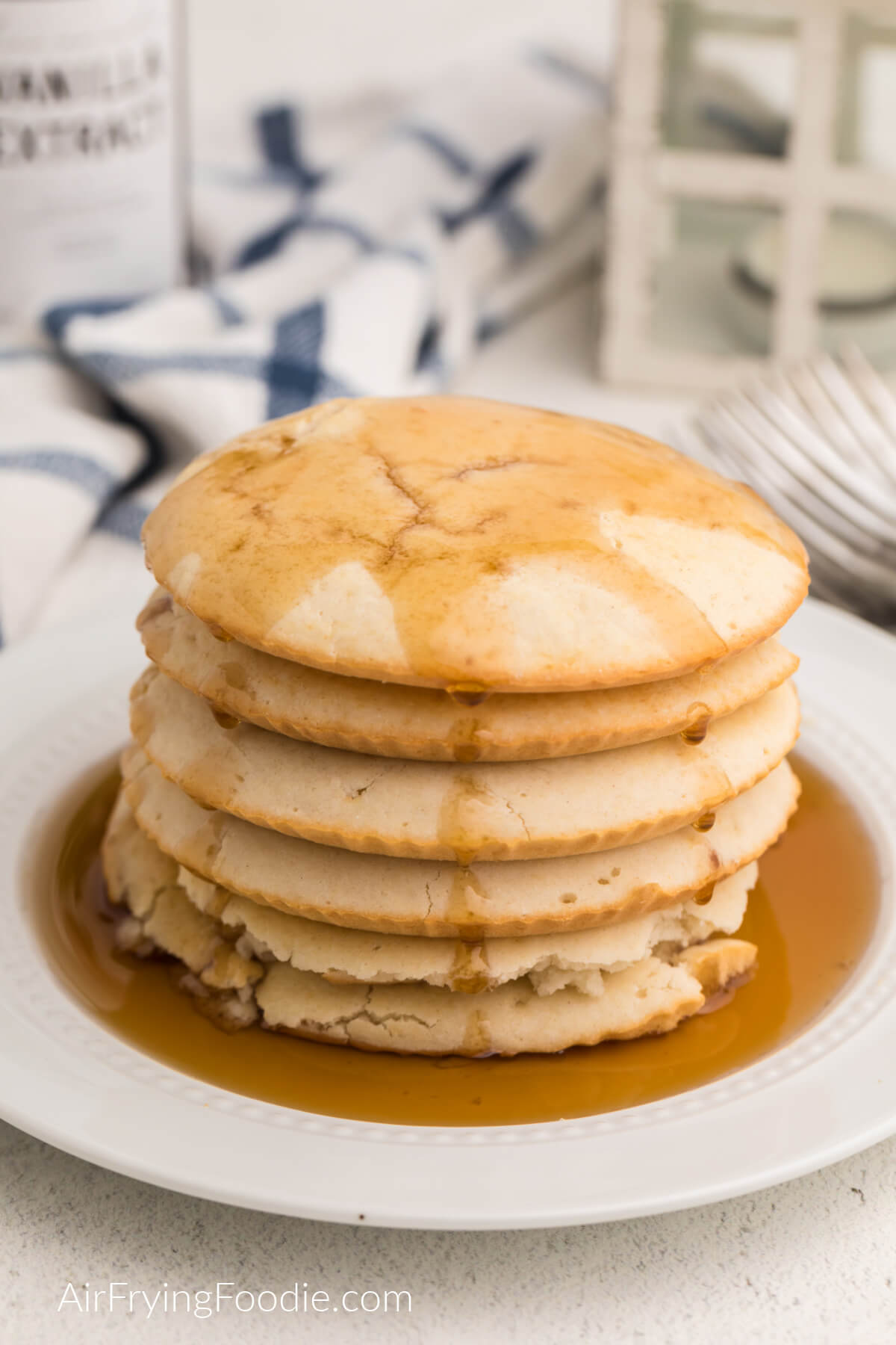 Fluffy pancakes made in the air fryer, stacked and served on a plate and topped with syrup. 