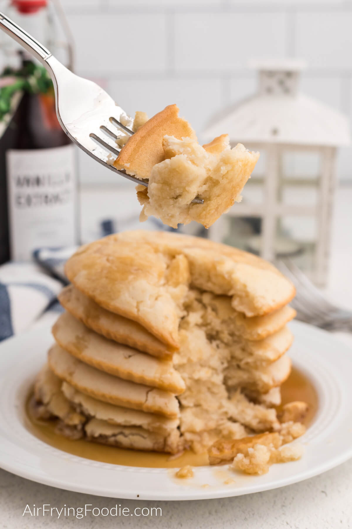 Bite of pancakes on a fork, taken from a stack of air fryer pancakes topped with syrup. 