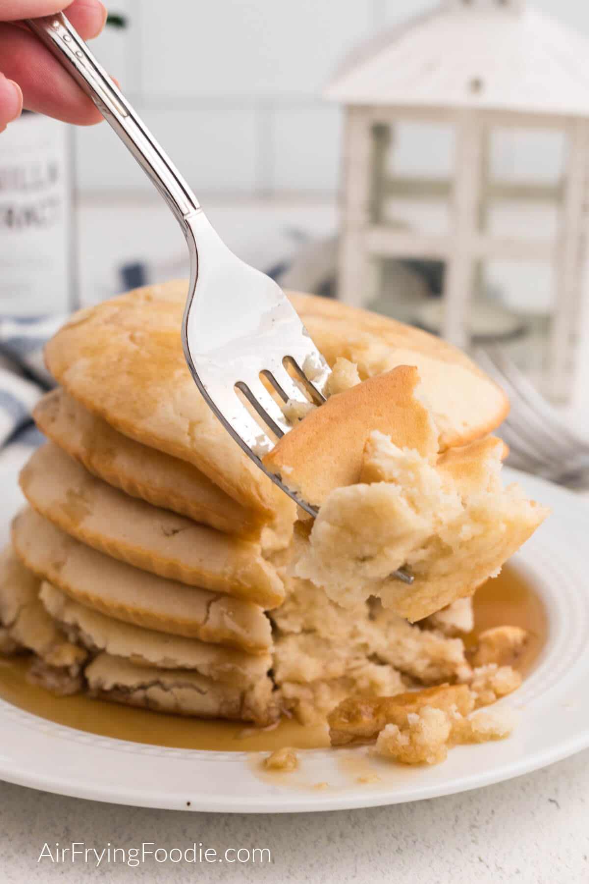Air fryer pancakes stacked on a plate, topped with syrup, and some on a fork for a bite. 