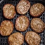 Juicy brown sausage patties in the air fryer basket after being cooked.