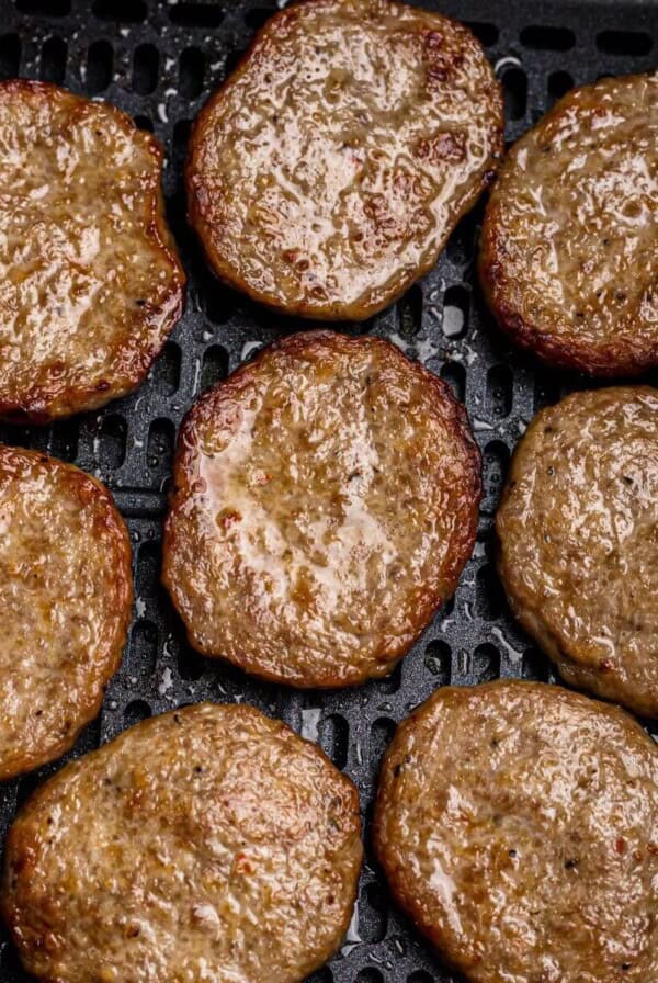 Juicy brown sausage patties in the air fryer basket after being cooked.