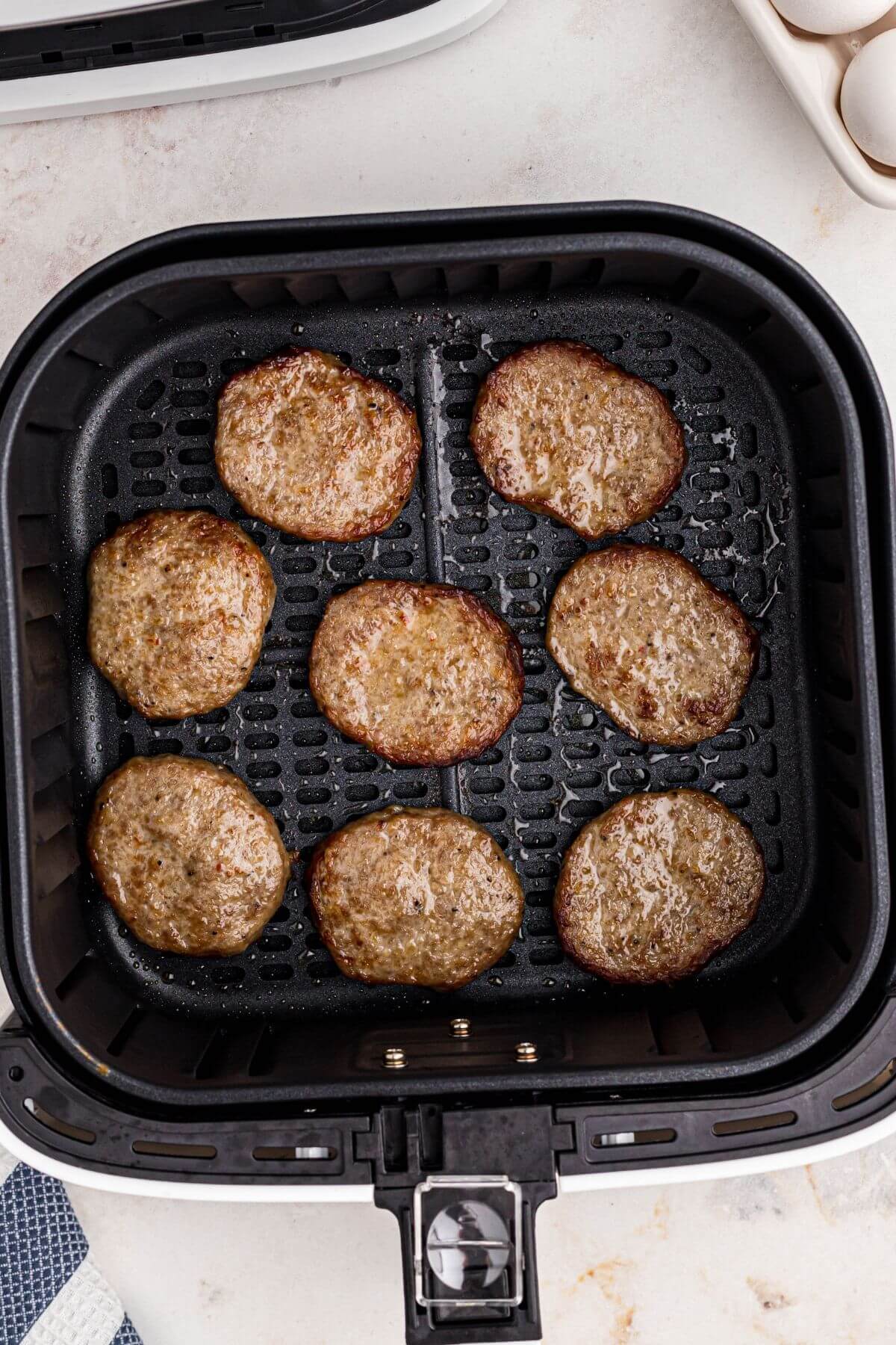 Juicy brown sausage patties in the air fryer basket after being cooked. 