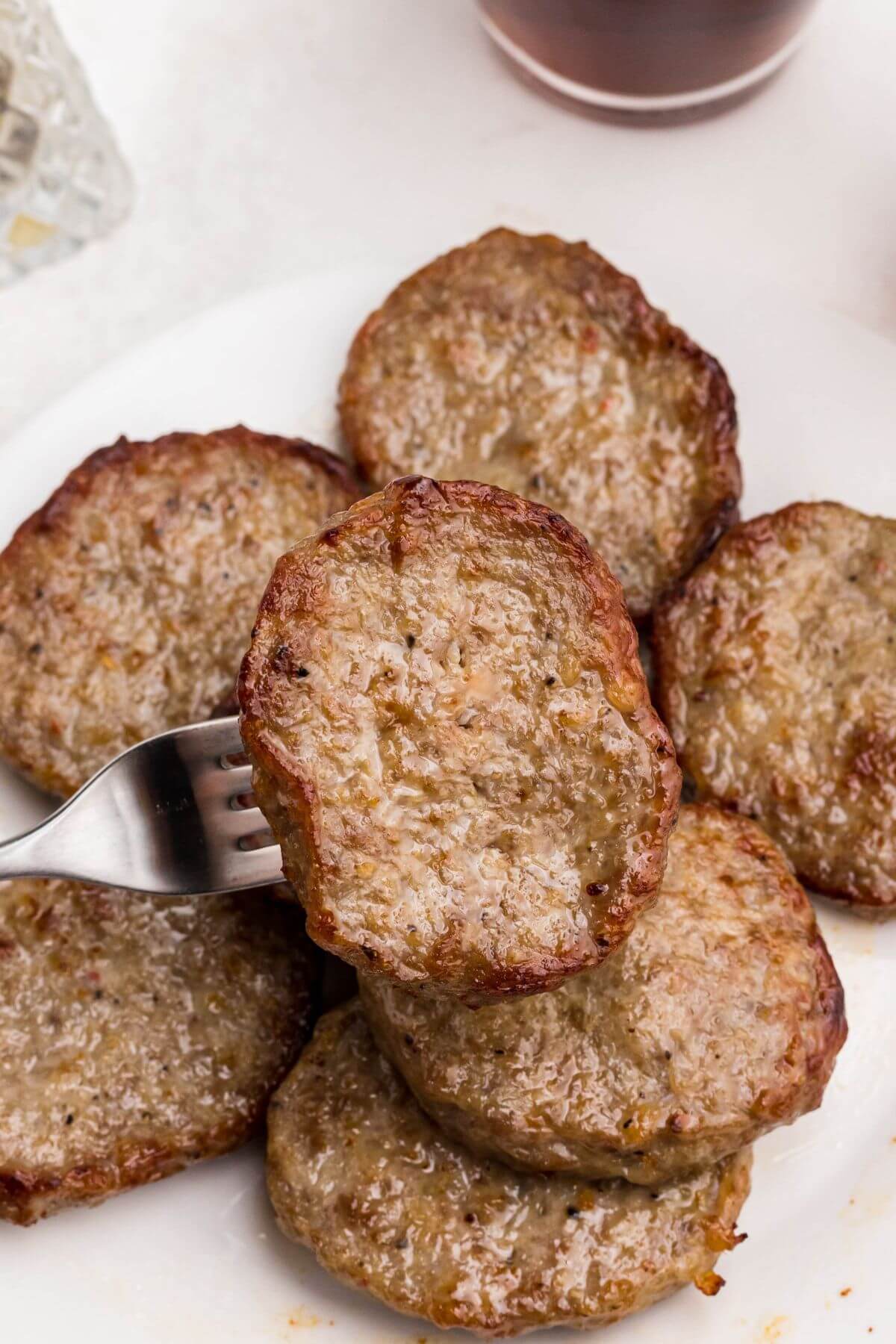 Golden brown and juicy sausage patties stacked on a plate with one being taken with a fork. 