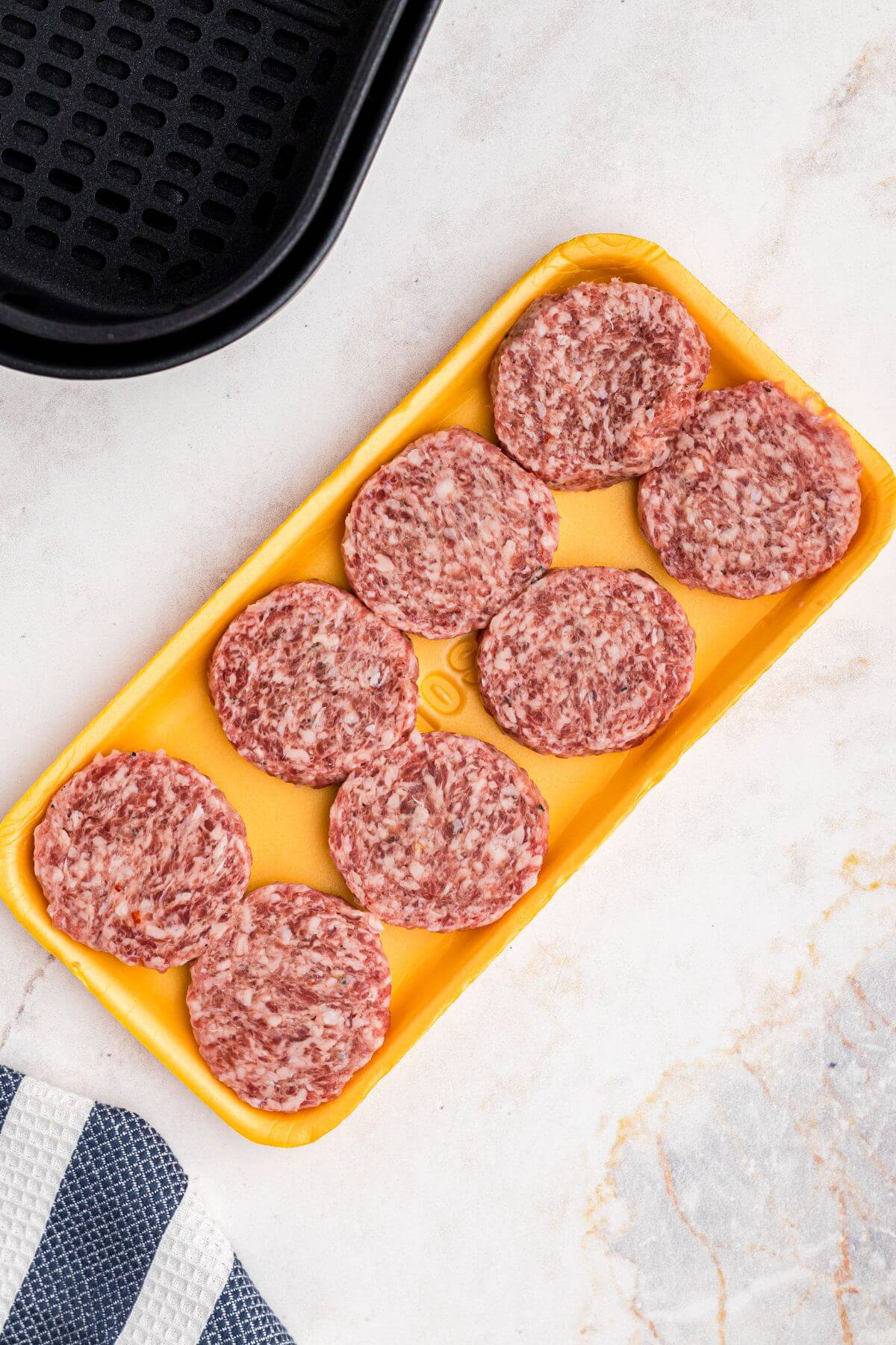 uncooked sausage patties in a yellow Styrofoam container on a marble table. 