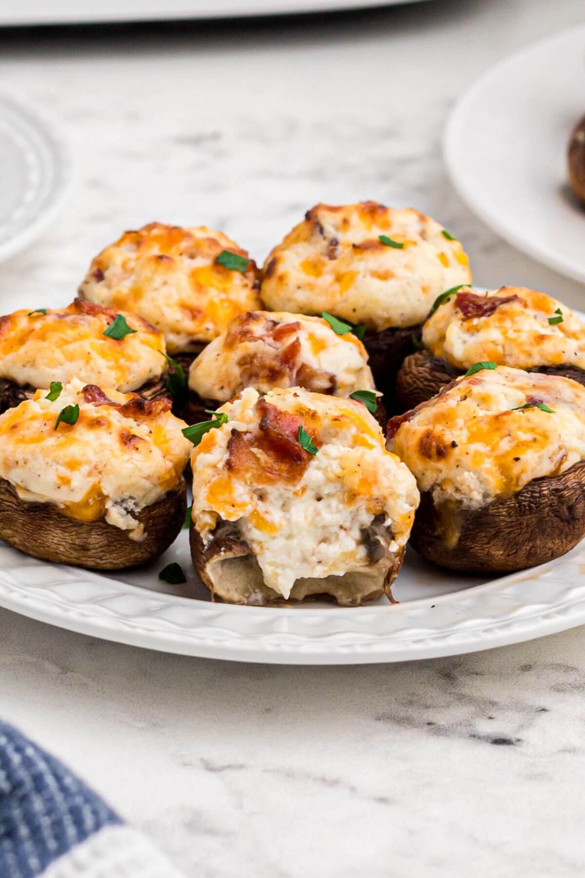 Golden brown mushrooms stuffed with cream cheese, cheddar cheese and bacon, on a small white plate. 