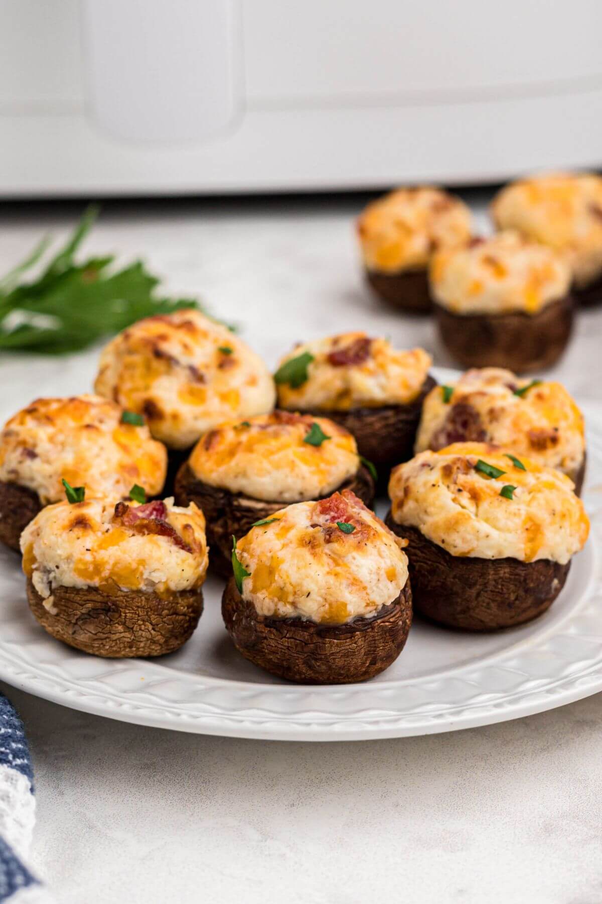 Golden brown stuffed mushrooms filled with cream cheese, cheese, and bacon, on a small white plate. 