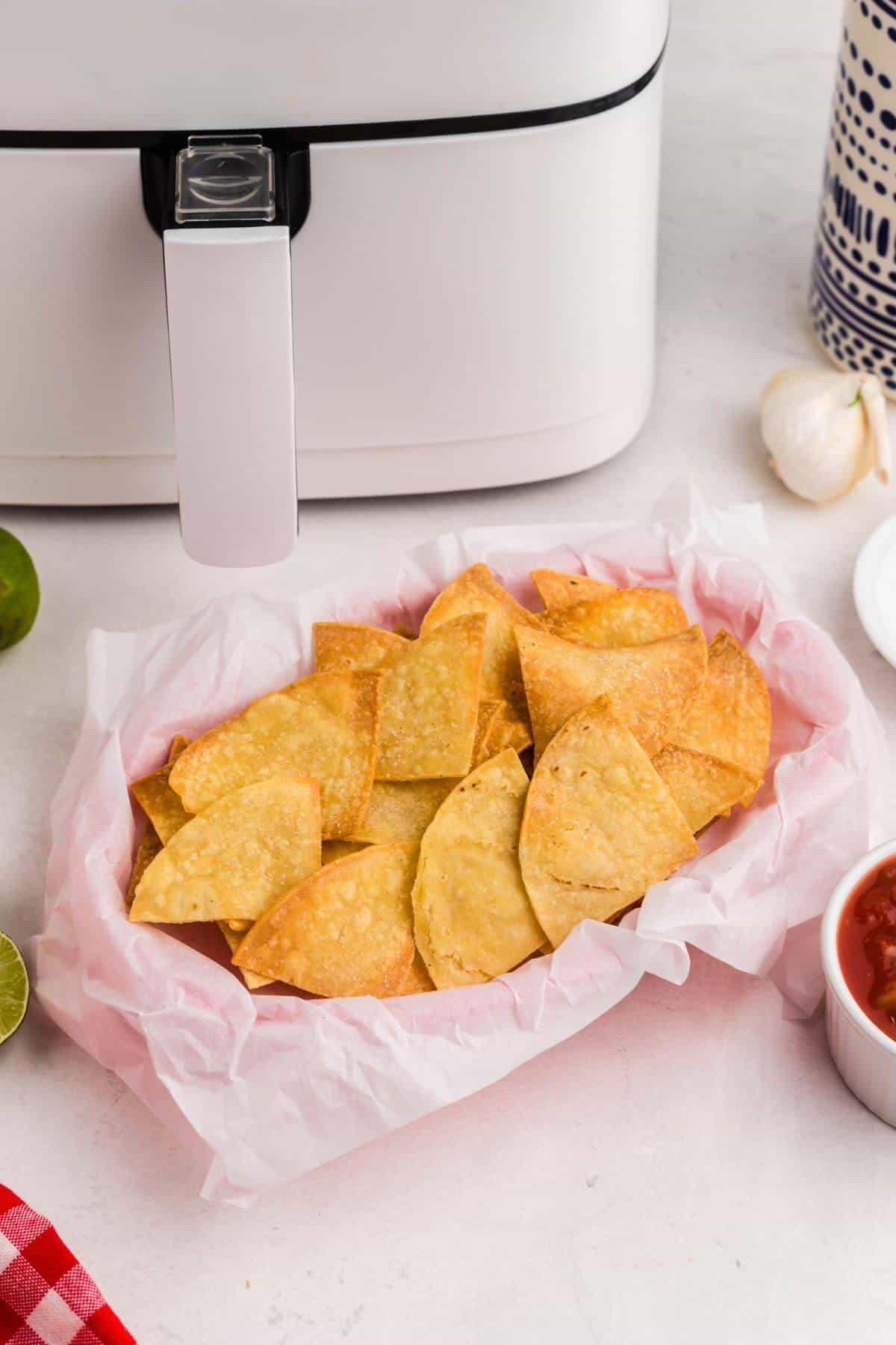 Golden crispy tortilla chips in a basket, in front of an air fryer. 