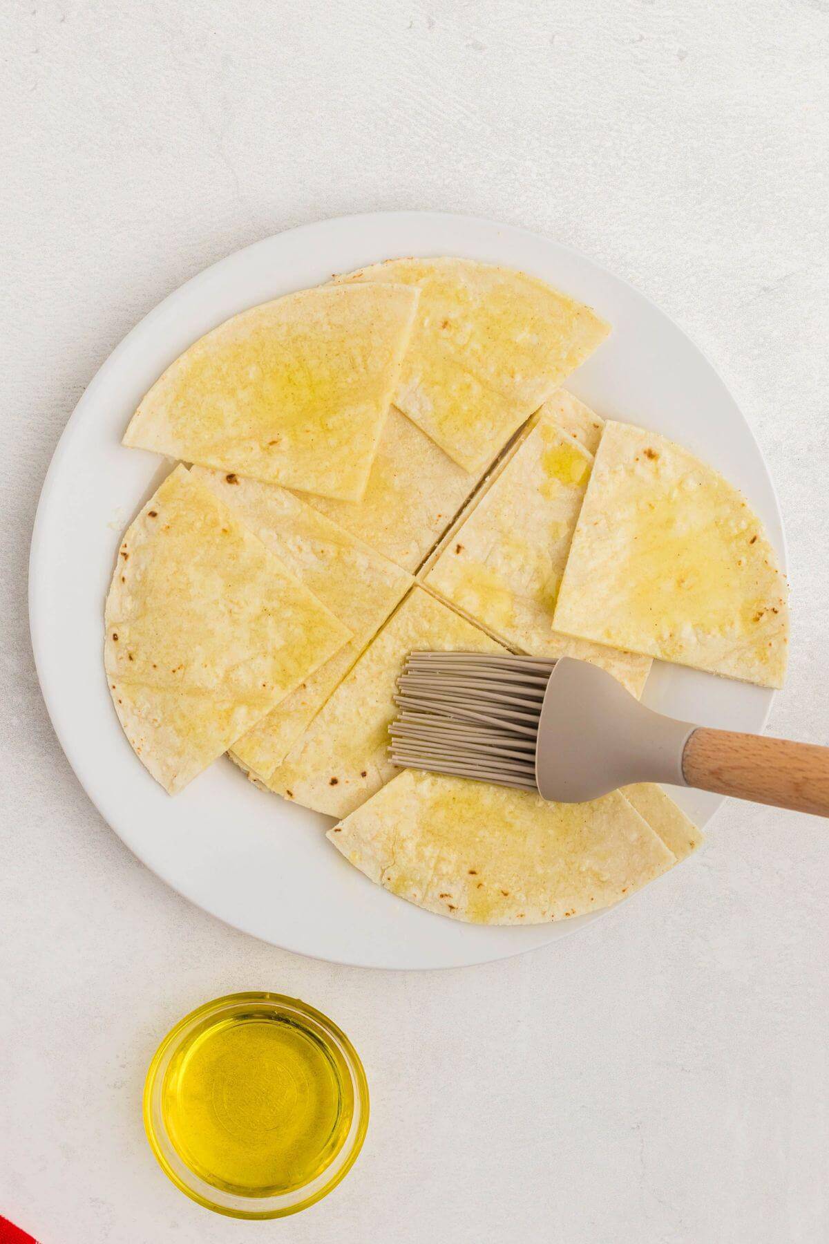 Pastry brush applying olive oil to slices of tortillas. 