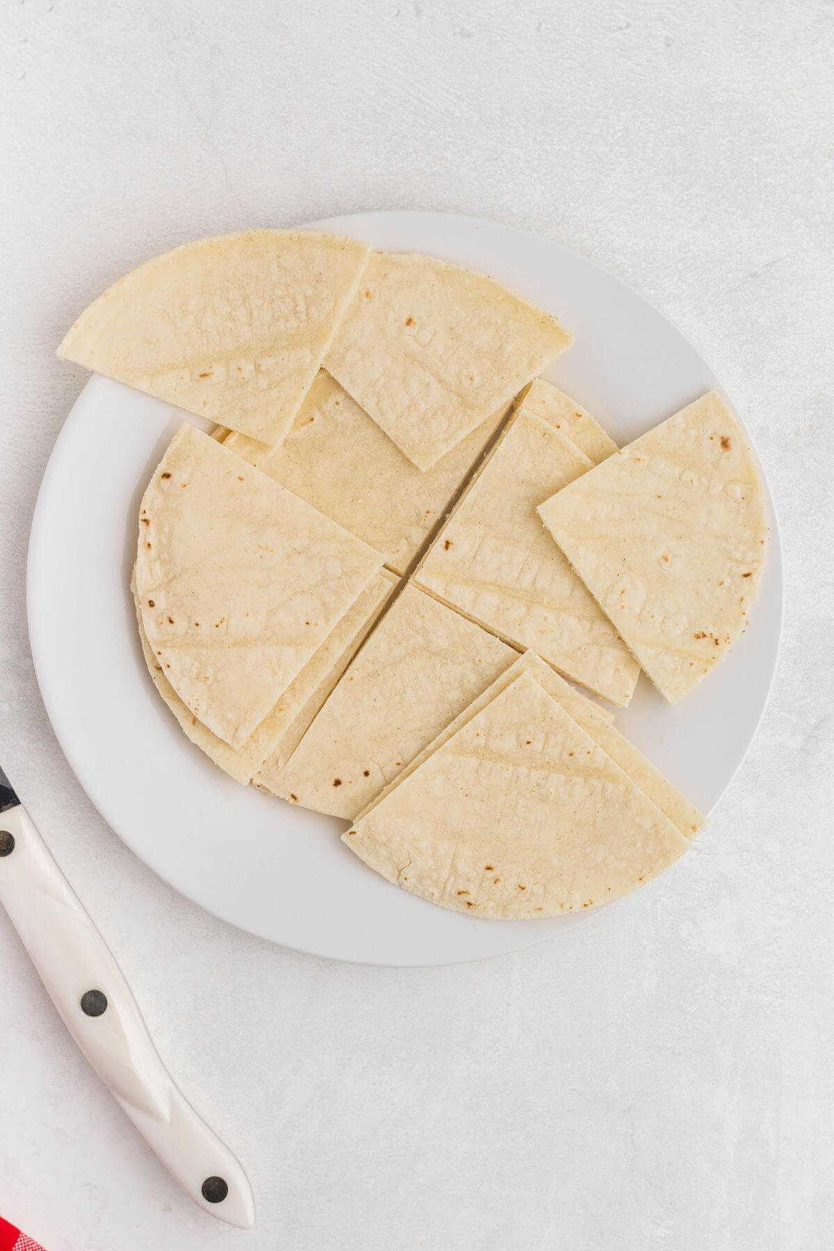 Tortillas on a white plate being cut into small triangles.  