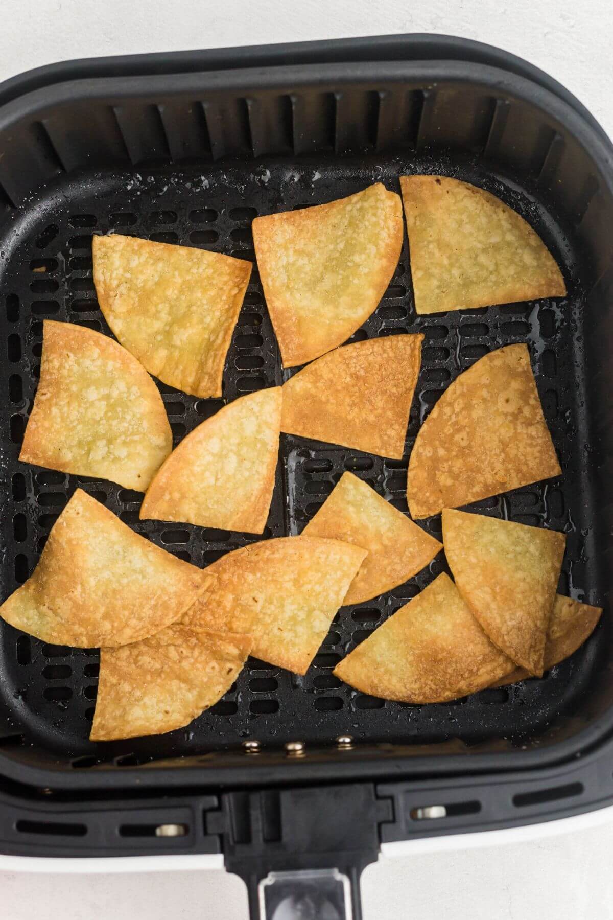 Golden crispy tortilla chips in the air fryer basket, after being air fried. 