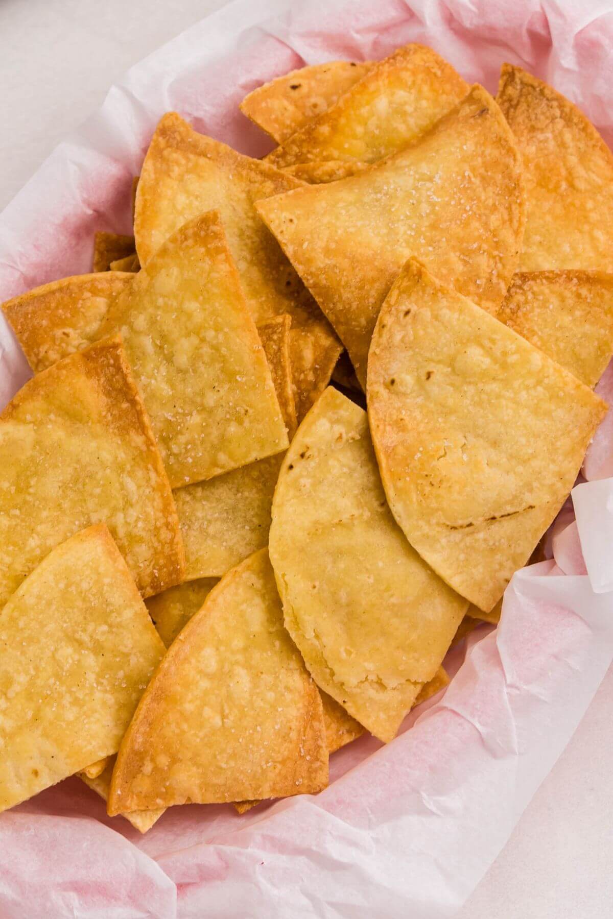Golden crispy tortilla chips seasoned with salt, piled into a small basked lined with parchment paper. 