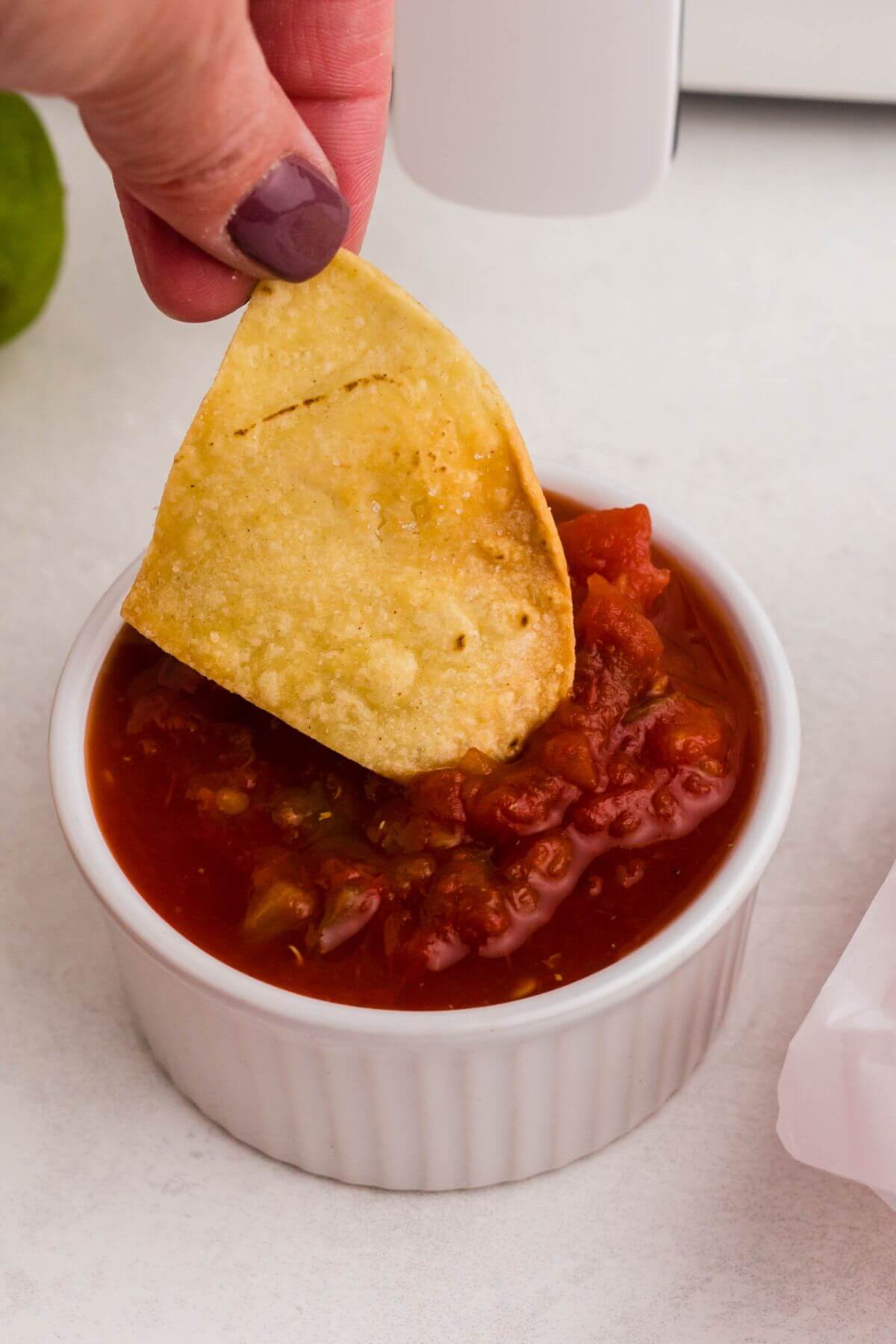 Golden tortilla chip being dipped into small ramekin of salsa. 