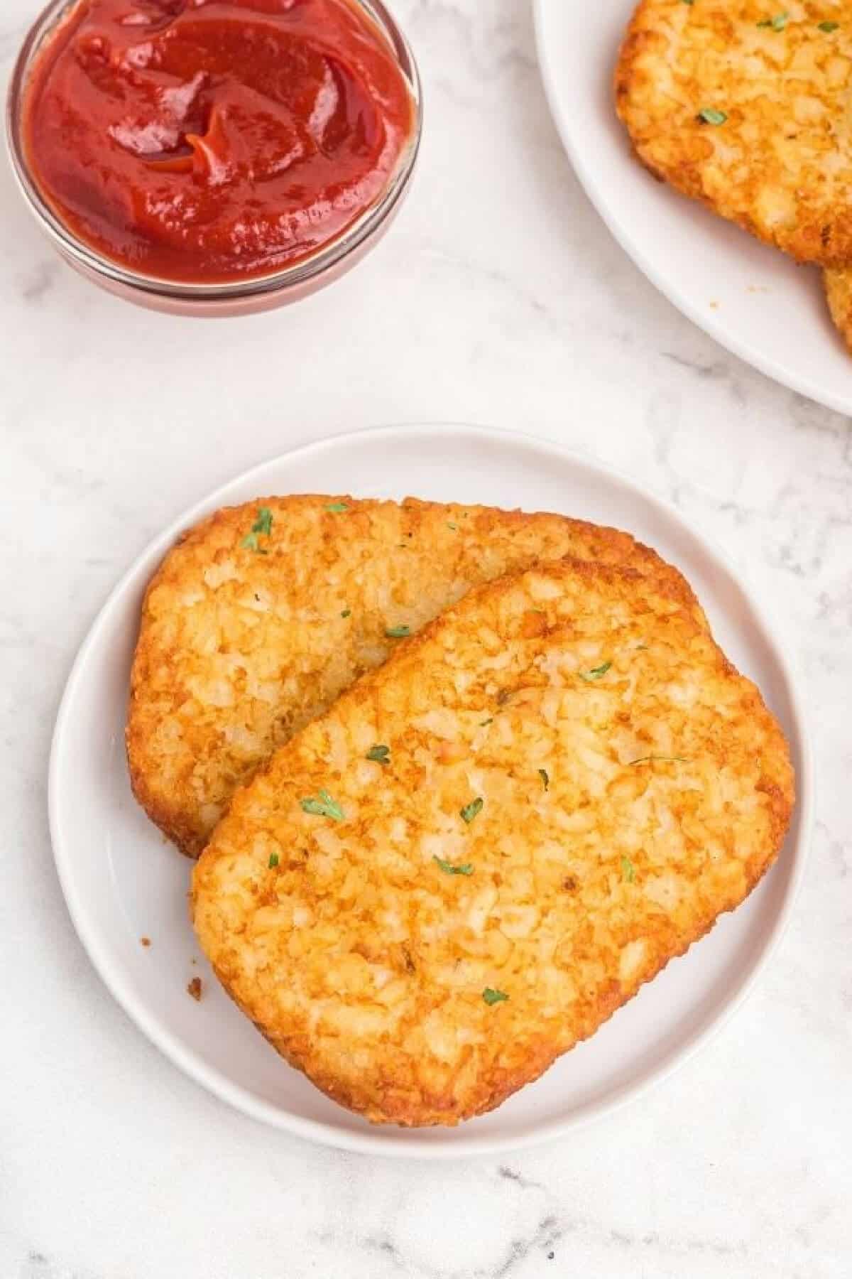 Hash brown patties on a white plate to serve after being cooked in the air fryer. 