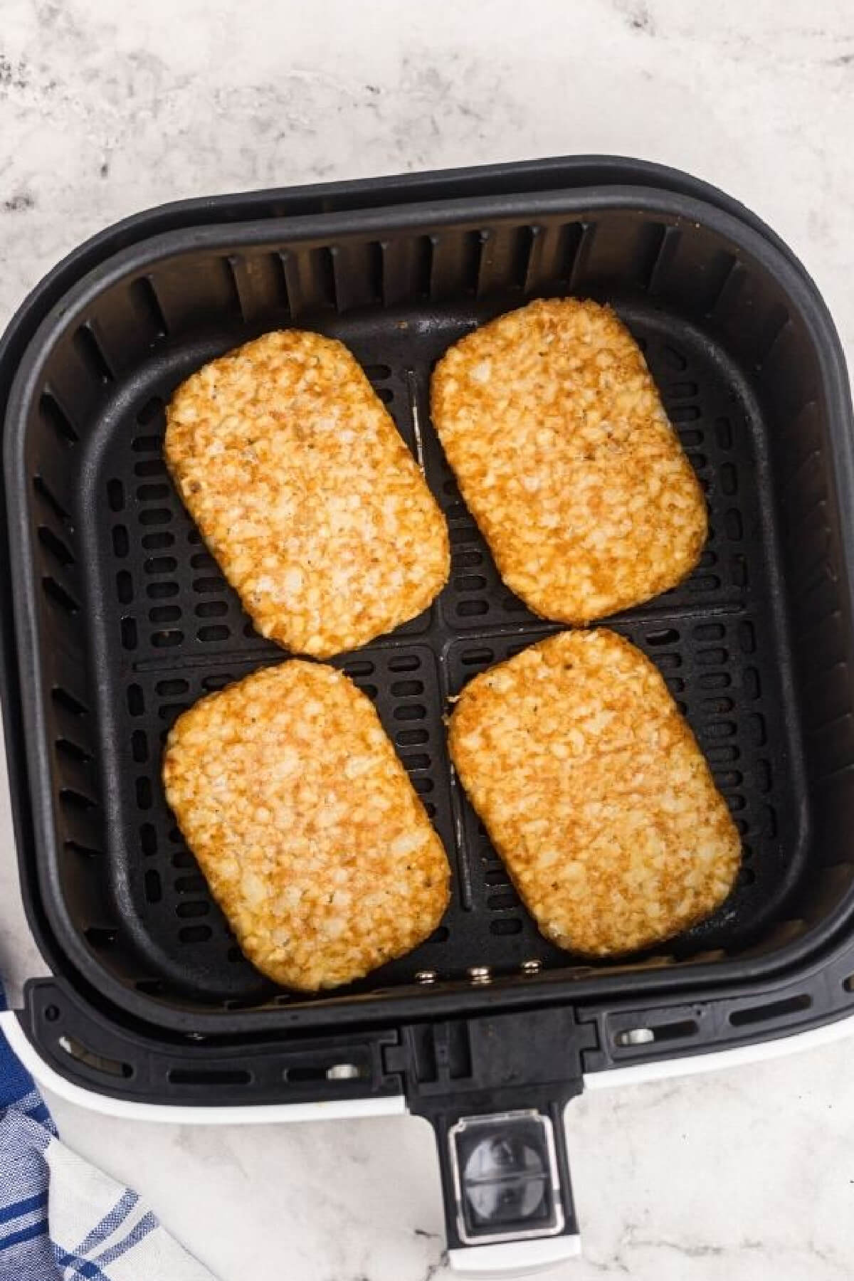 Frozen hash browns in air fryer basket ready to cook. 