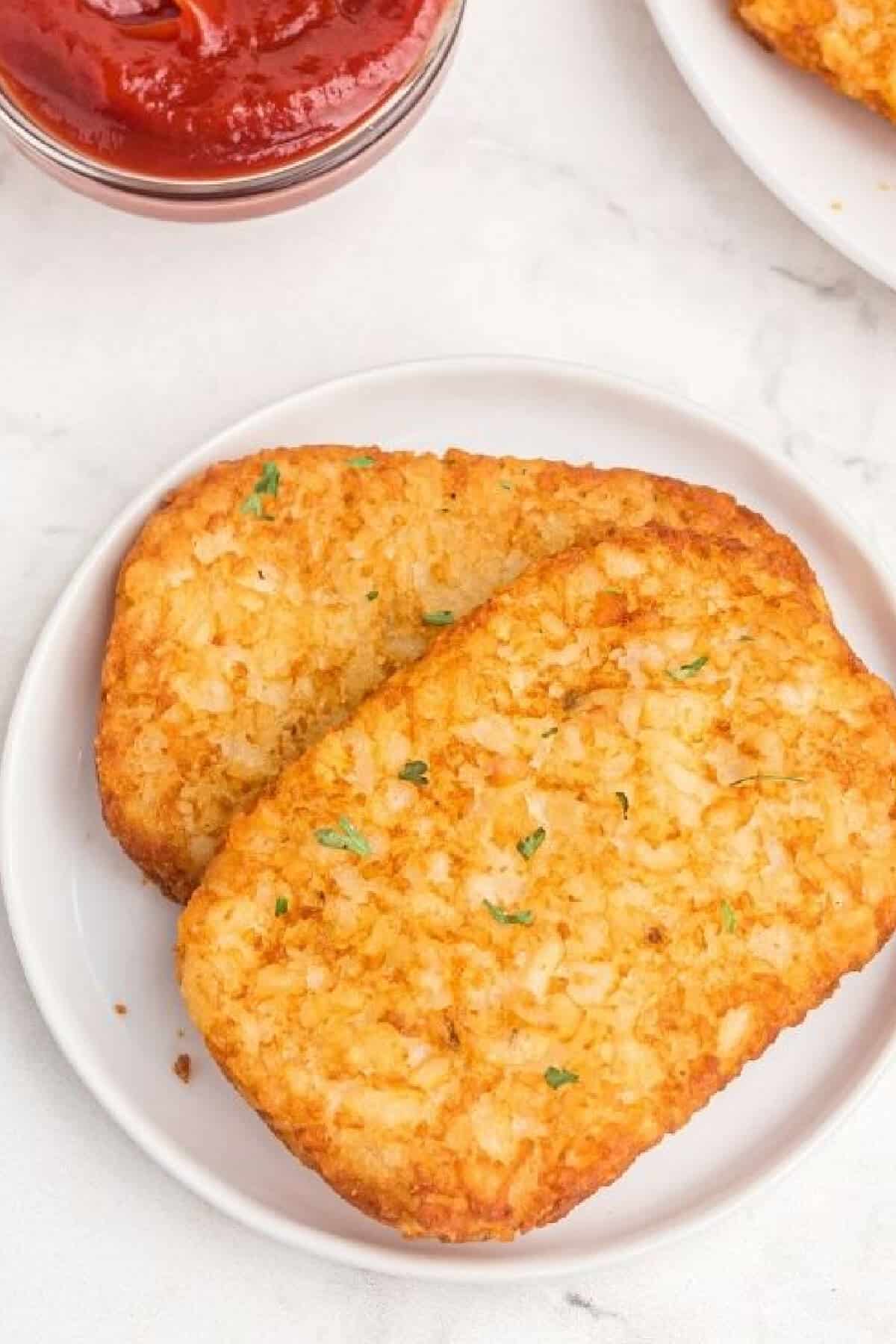 Two hash browns that were cooked in the air fryer on a white plate ready to eat. 