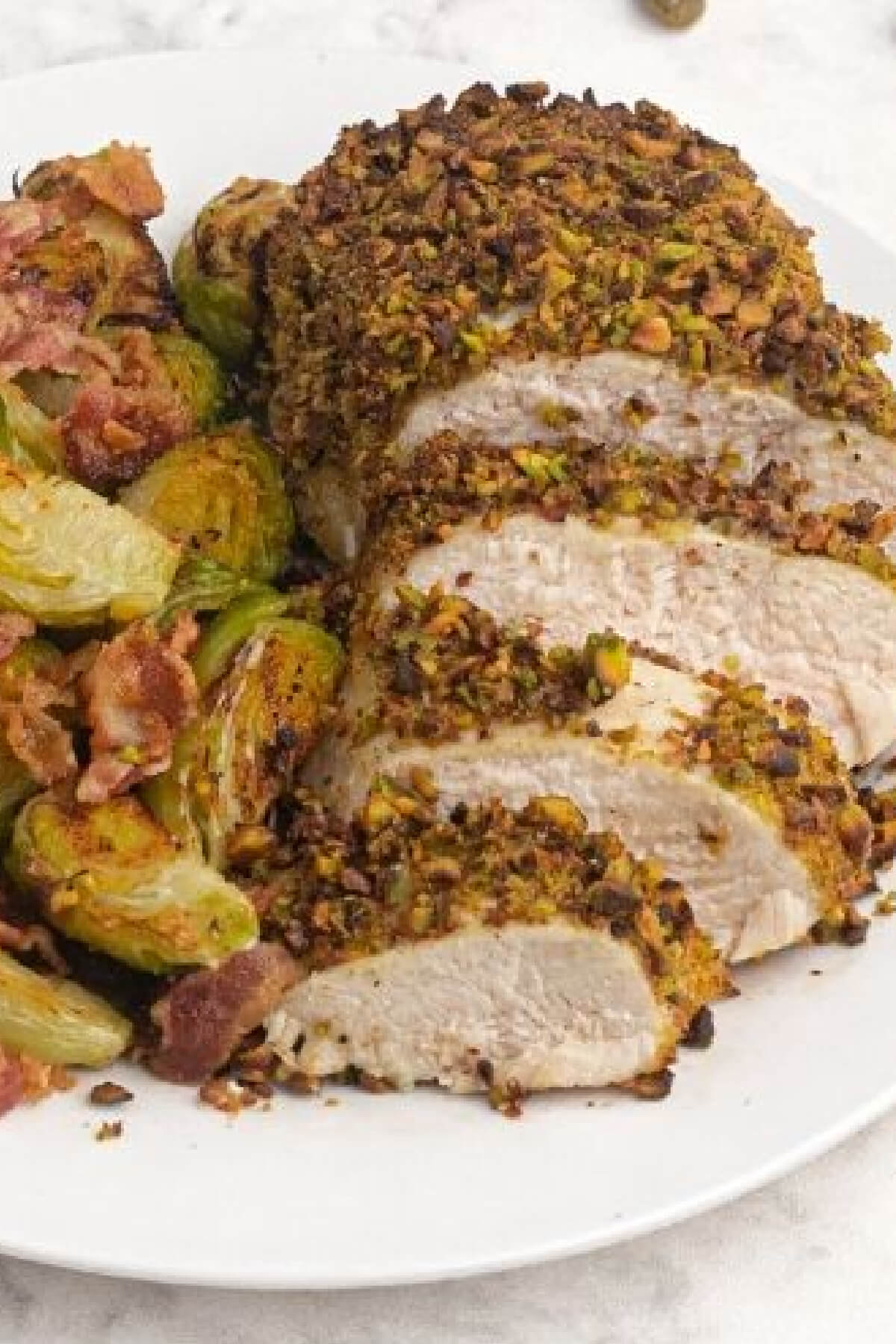 air fryer pistachio crusted chicken on a white plate with brussel sprouts and bacon. 