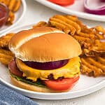 reheated burger in a air fryer, topped with cheese and other toppings, served on a white plate with waffle fries.