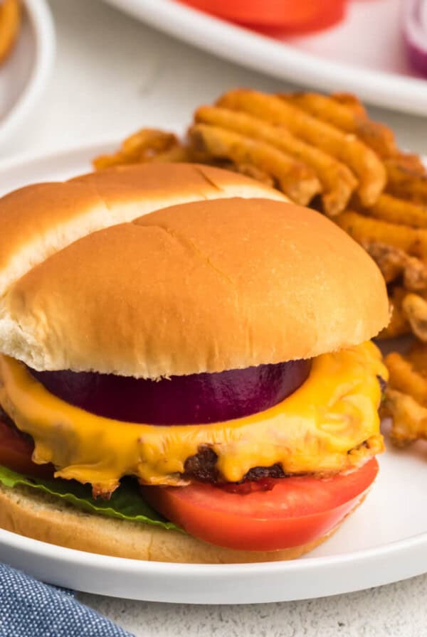 reheated burger in a air fryer, topped with cheese and other toppings, served on a white plate with waffle fries.