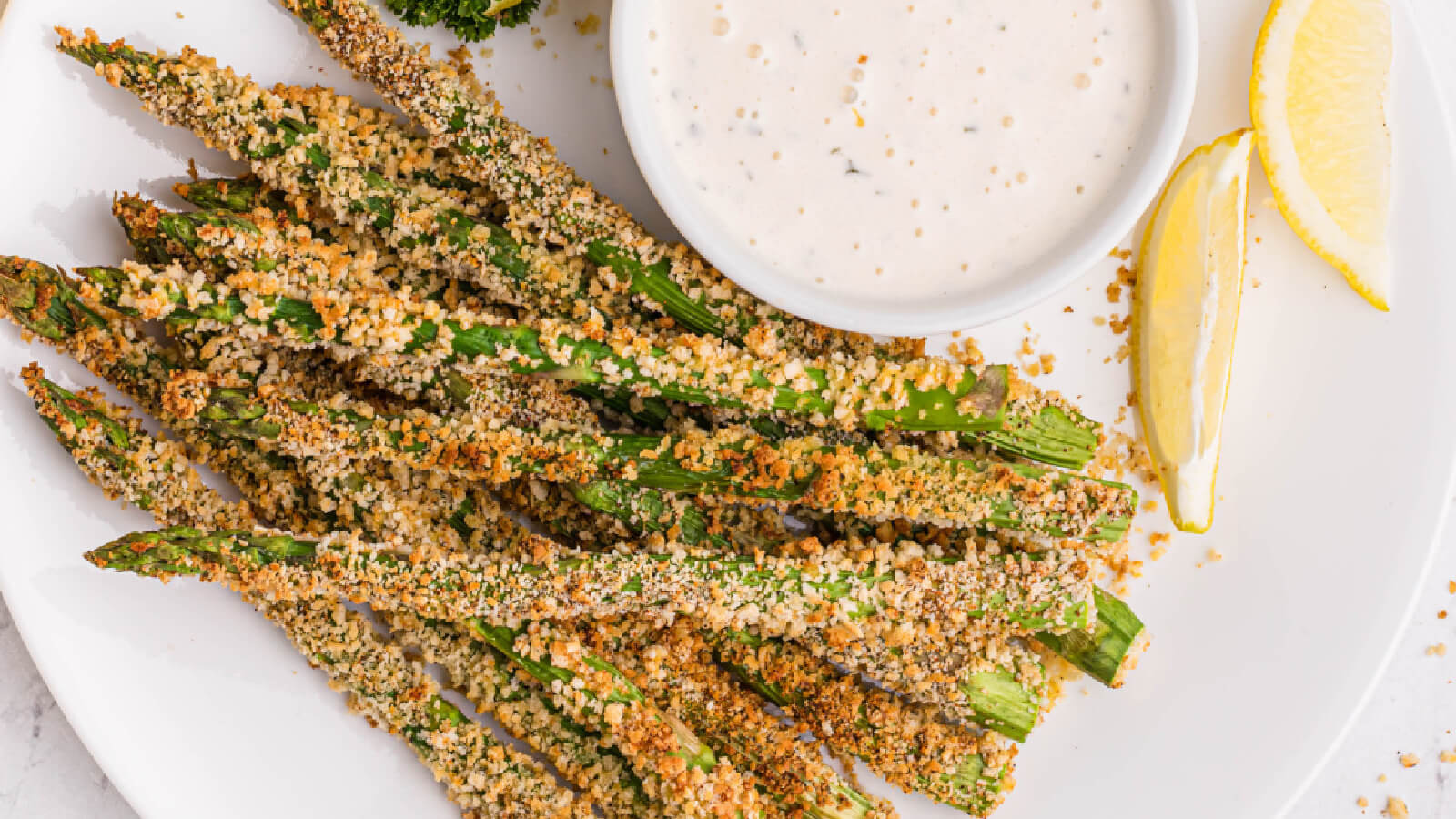 Air fryer asparagus fries on a white plate with a small bowl or dressing to dip them in.