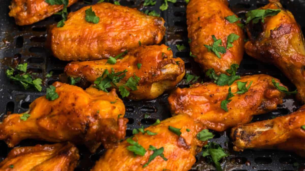 crispy chicken wings in the air fryer basket topped with fresh parsley.