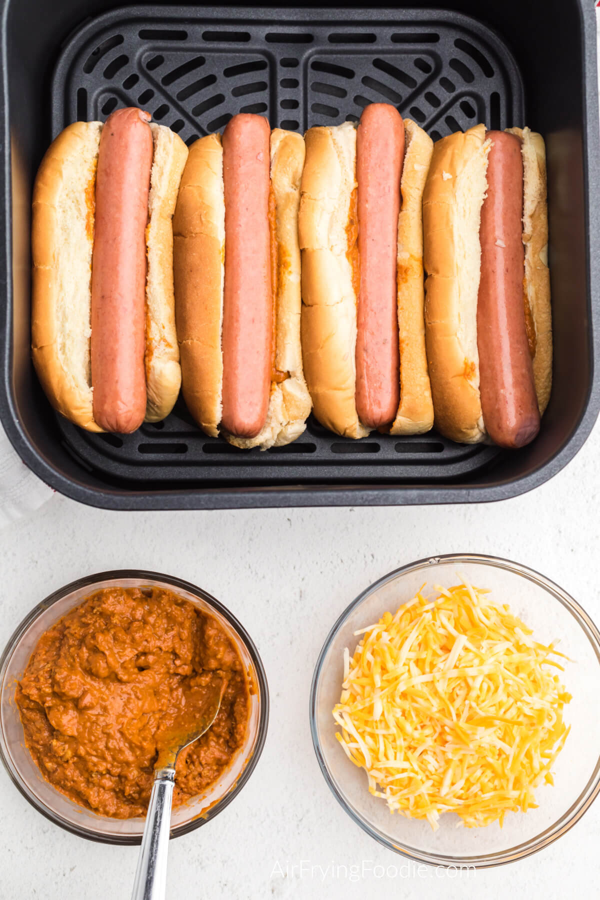 Hot dogs added to the buns with chili in the air fryer basket. 