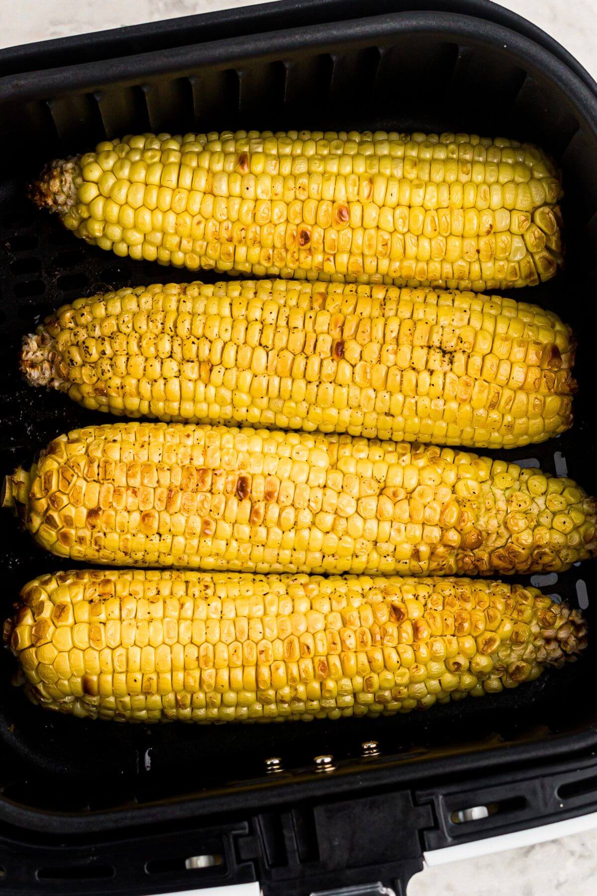 Golden yellow cooked ears of corn in the air fryer basket. 