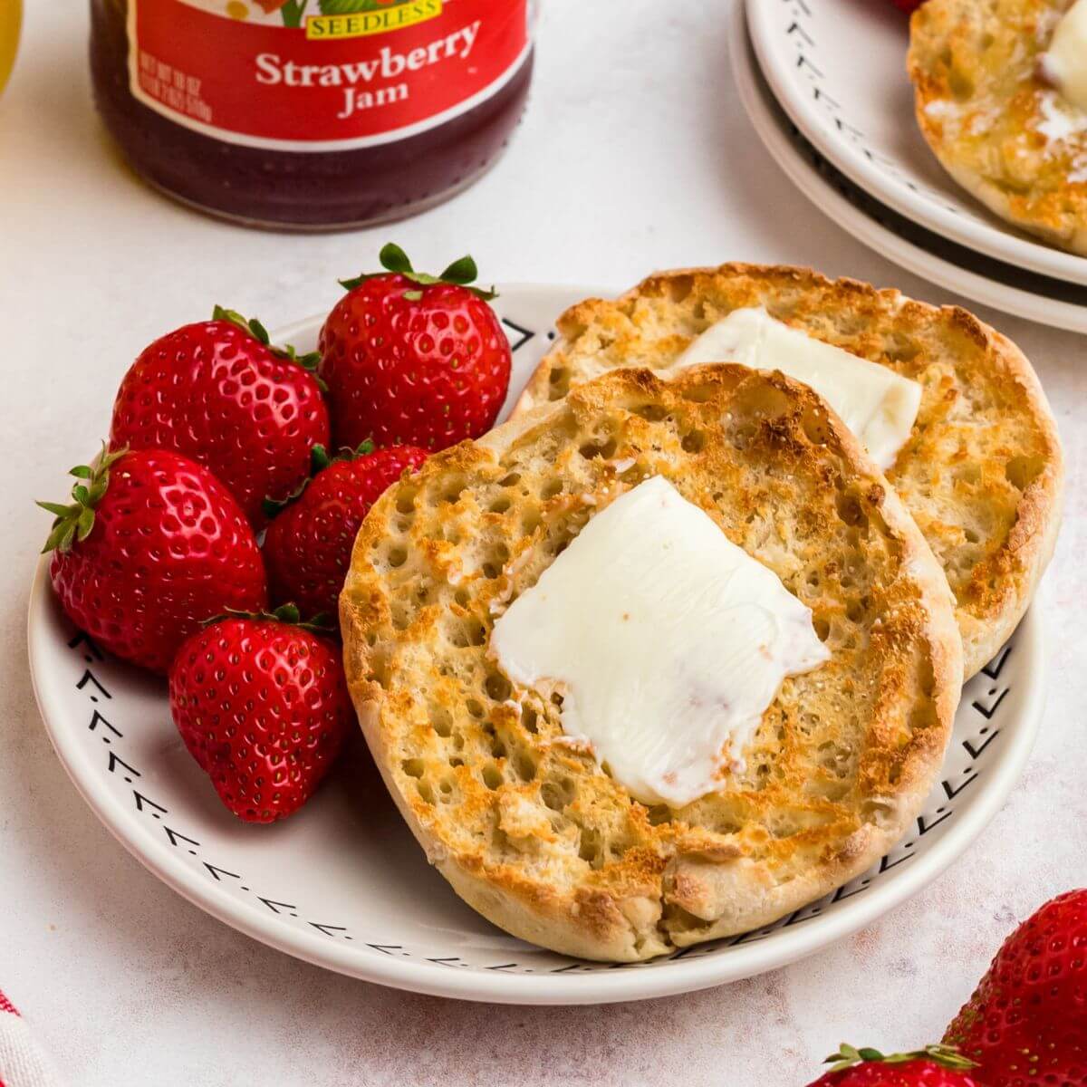 Golden crispy English muffins with a piece of butter on top, on a white plate served with strawberries and orange juice.