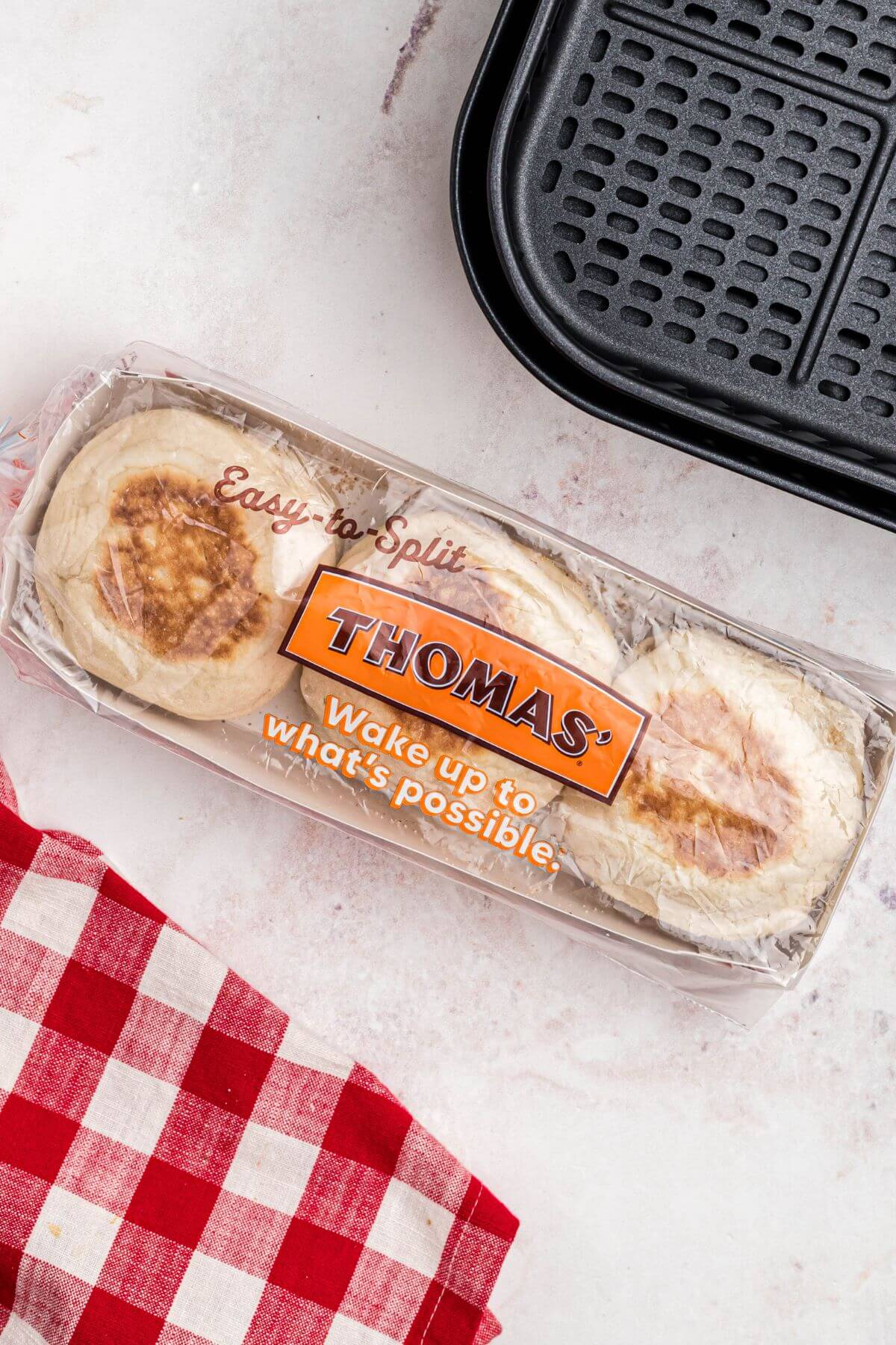 Package of English muffins on a marble table with a red checkered linen.