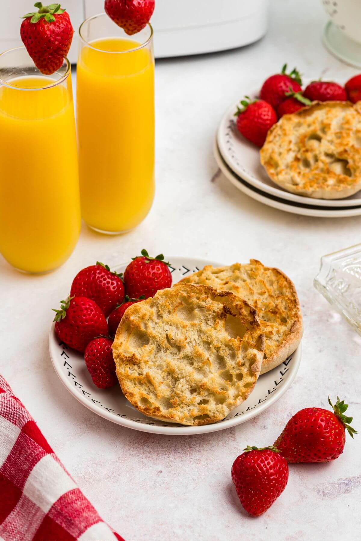 Golden crispy English muffins on a white plate served with strawberries and orange juice.