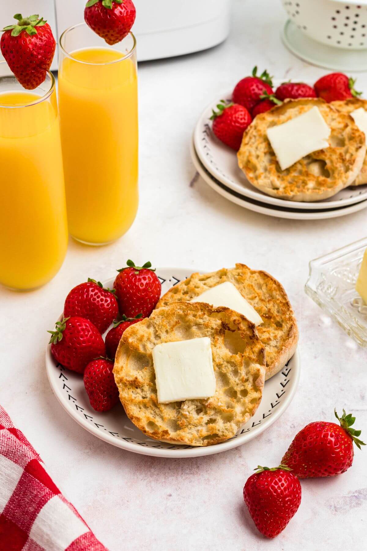 Golden crispy English muffins on a white plate served with strawberries and orange juice. 