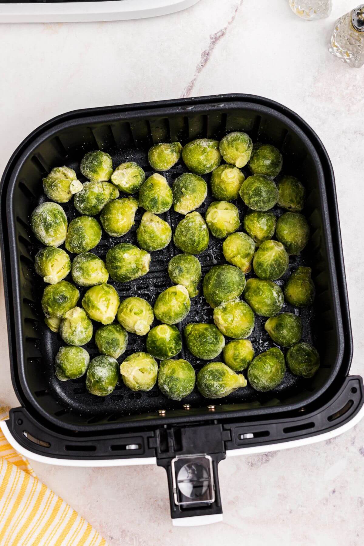 Frozen brussels sprouts in the air fryer basket before being cooked. 