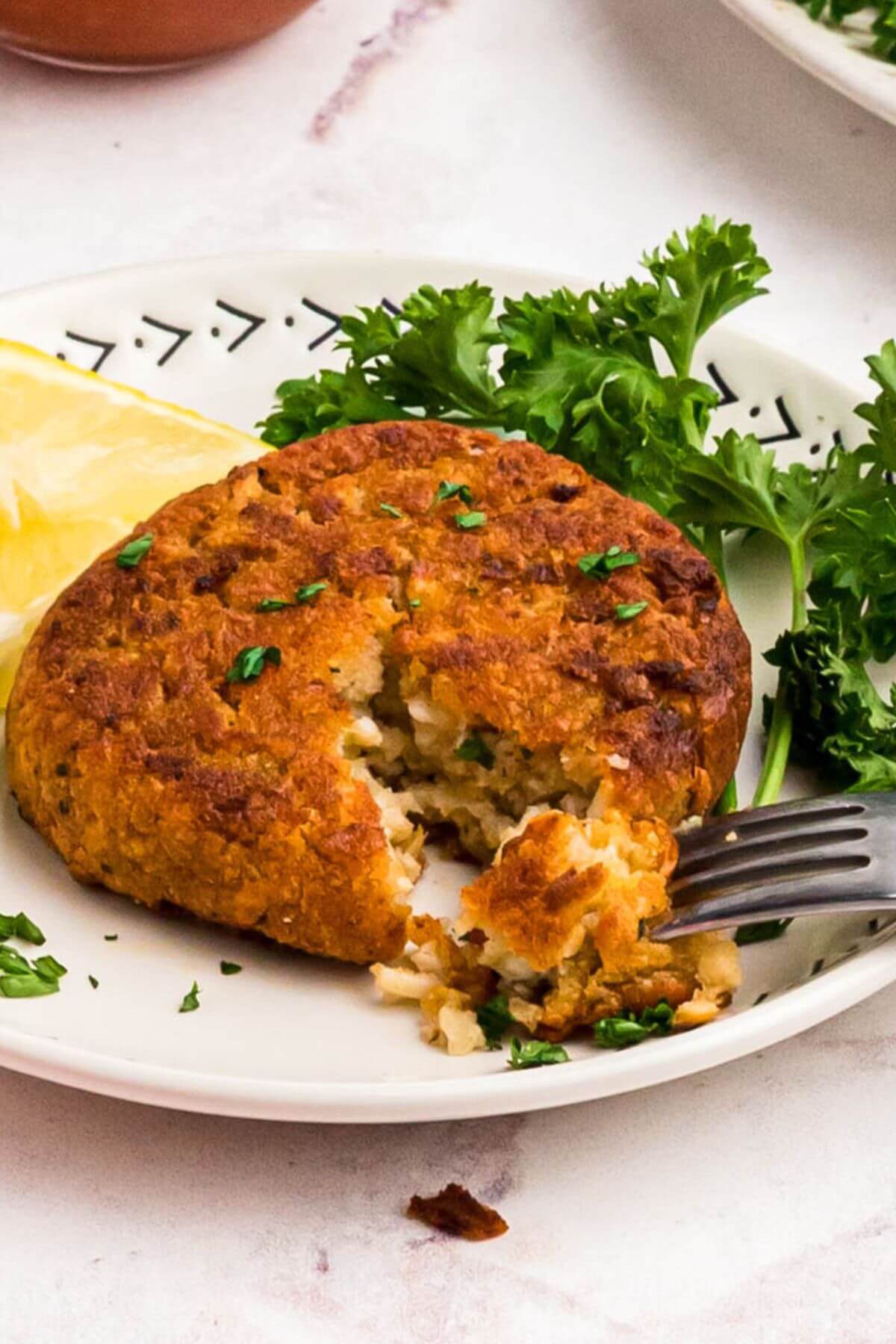 Golden crispy crab cake on a small plate with a fork taking a small piece. 
