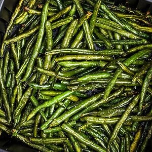 Seasoned green beans in the air fryer basket after being cooked.