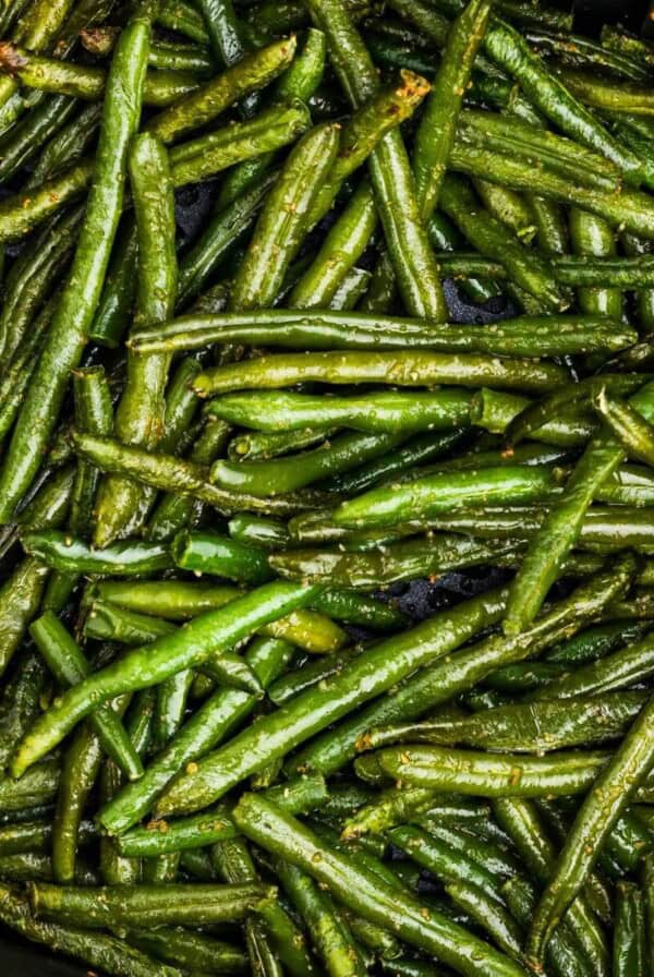 Seasoned green beans in the air fryer basket after being cooked.