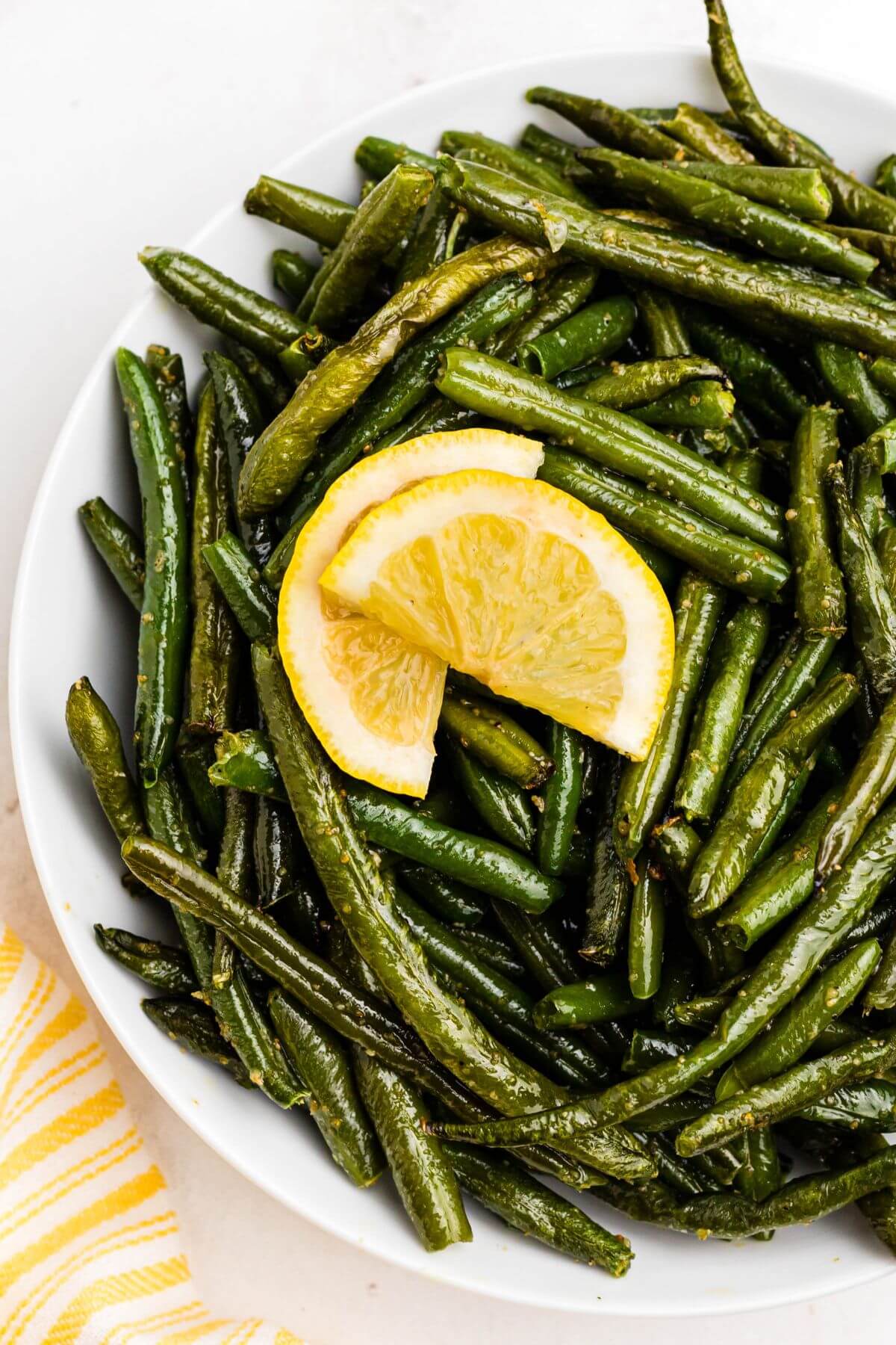 Juicy green beans in a white bowl topped with lemon wedges.