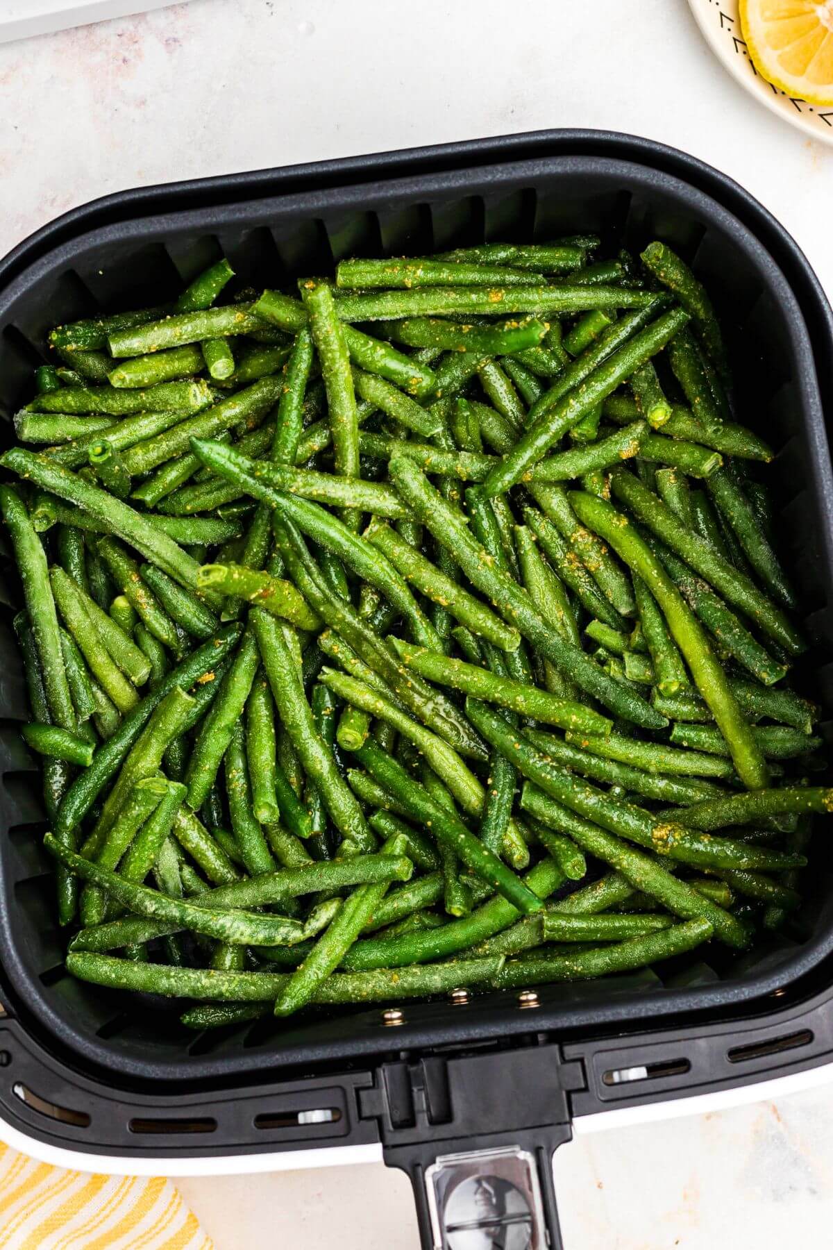 Seasoned frozen green beans in the air fryer basket. 