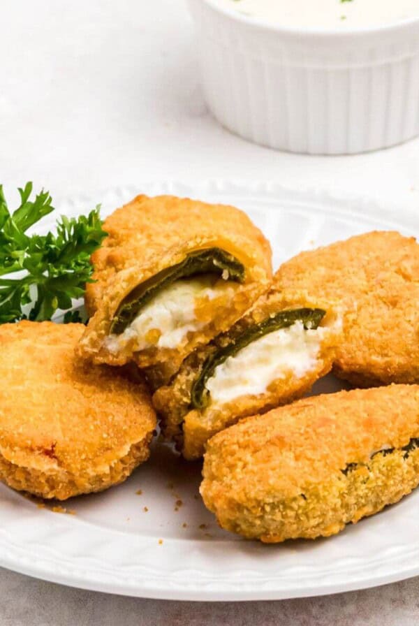 Golden crispy breaded jalapeno poppers on a small white plate.