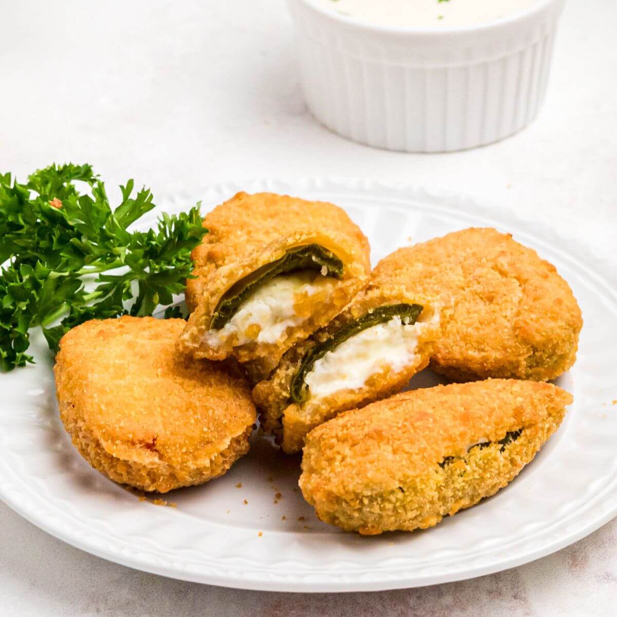 Golden crispy breaded jalapeno poppers on a small white plate.