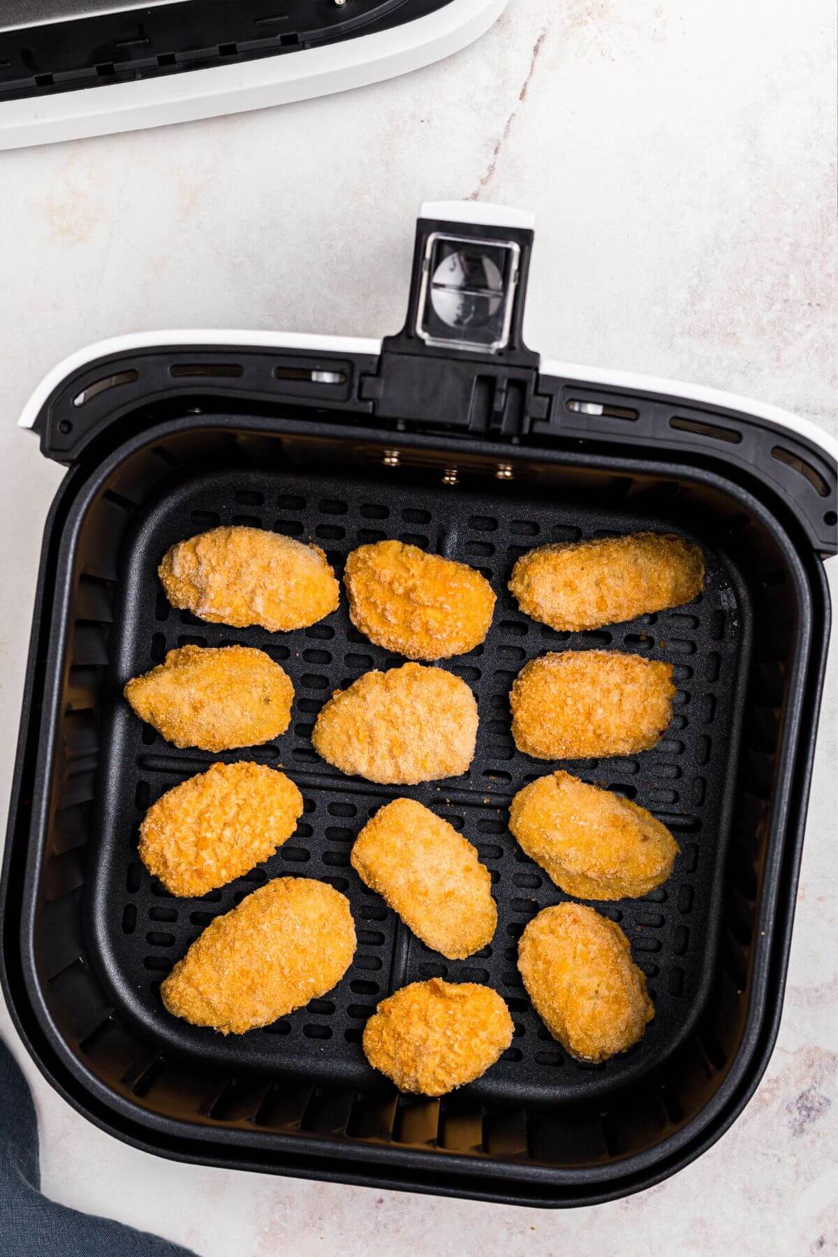Frozen jalapeno poppers in an air fryer basket before being cooked. 