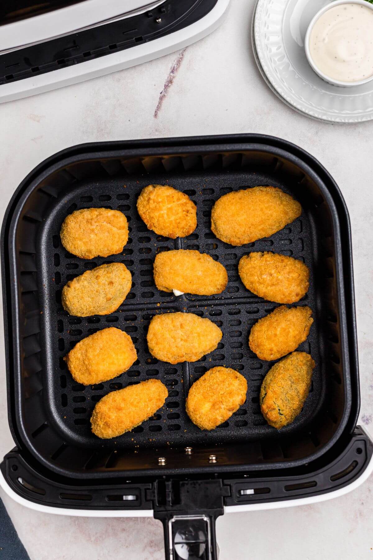Golden crispy breaded jalapeno poppers in the air fryer basket after being cooked. 