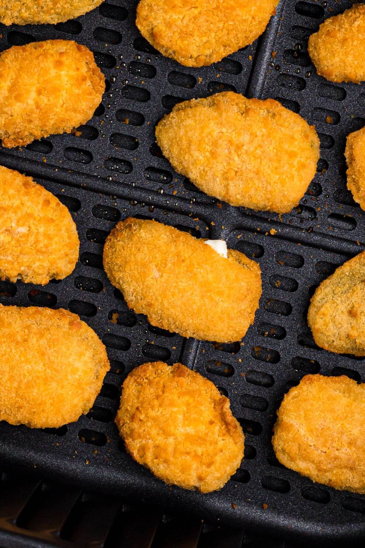 Golden crispy breaded jalapeno poppers in the air fryer basket after being cooked.